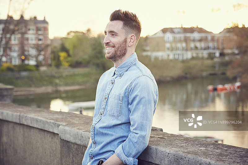 倚靠在英国里士满泰晤士河桥上的年轻胡子男人图片素材