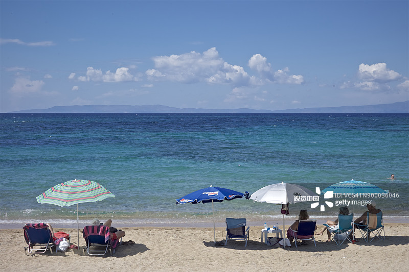 在希腊纳夫普利奥海滩的遮阳伞下放松身心，欣赏克里特海的碧蓝海水图片素材