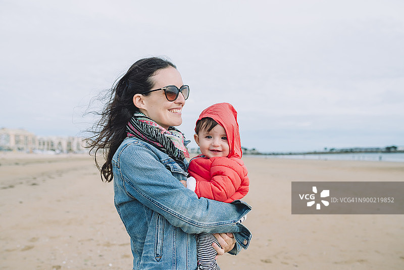 海滩上母亲怀里微笑的女婴肖像图片素材
