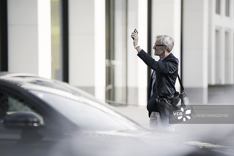 在城市里打电话叫出租车的灰发商人图片素材