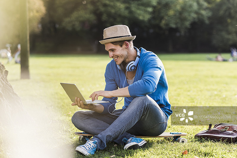 在公园里使用笔记本电脑的滑板少年图片素材