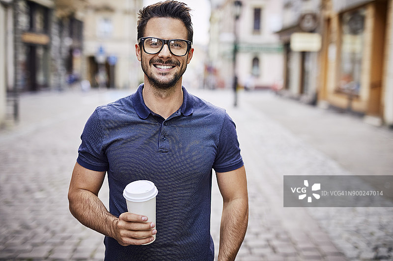 一个戴着眼镜在户外喝咖啡的微笑男人的肖像图片素材