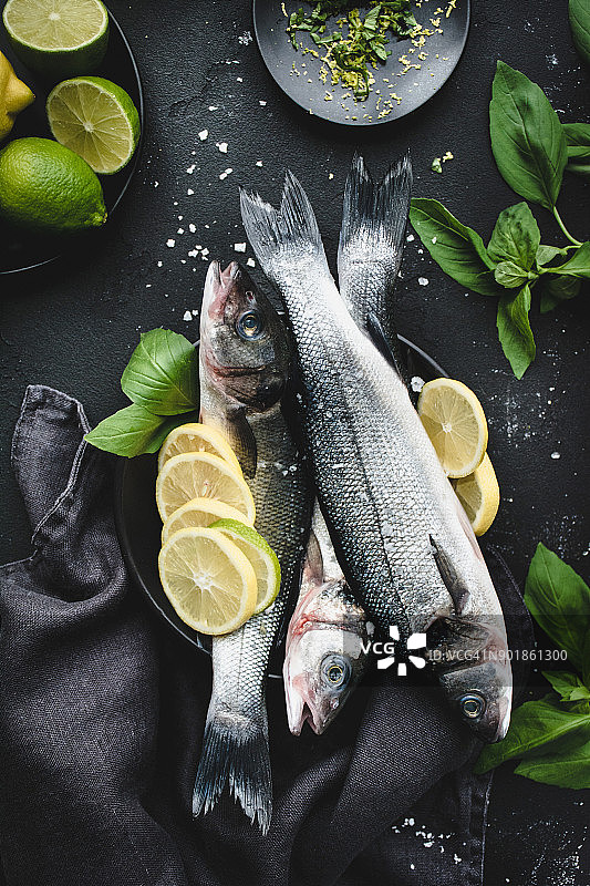 新鲜鱼配柠檬、香料和草药，可用于深色背景烹饪图片素材