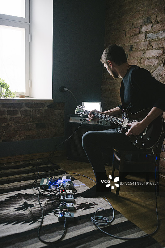 年轻音乐家看着平板电脑在放大器上弹吉他图片素材