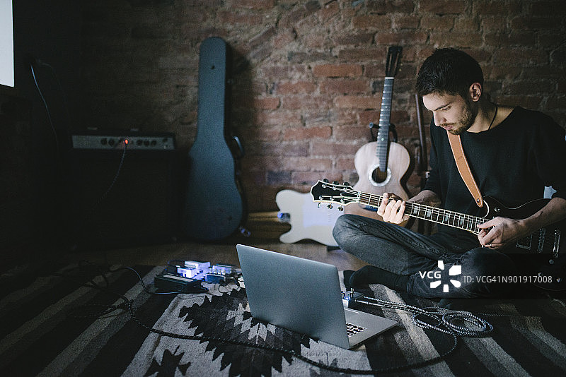 年轻音乐家坐在笔记本前弹吉他图片素材