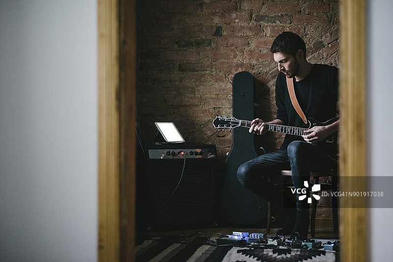 年轻音乐家在另一个房间弹吉他，平板电脑放在放大器上图片素材