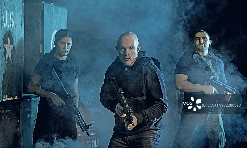 在黑暗的室内城市环境中摆姿势的武装格斗团体图片素材