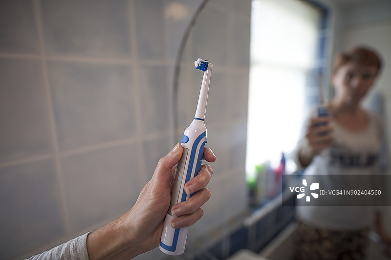 女士在浴室用电动牙刷刷牙图片素材