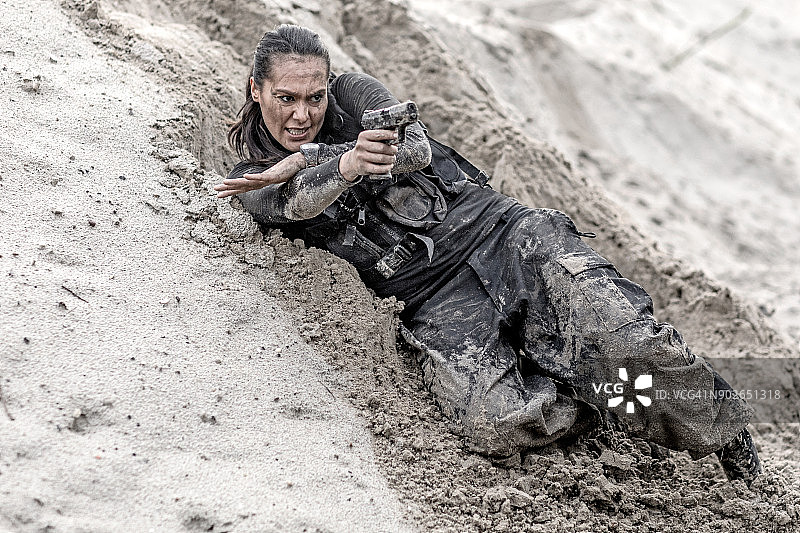 在泥泞的沙地里训练时使用武器的漂亮棕发女兵图片素材