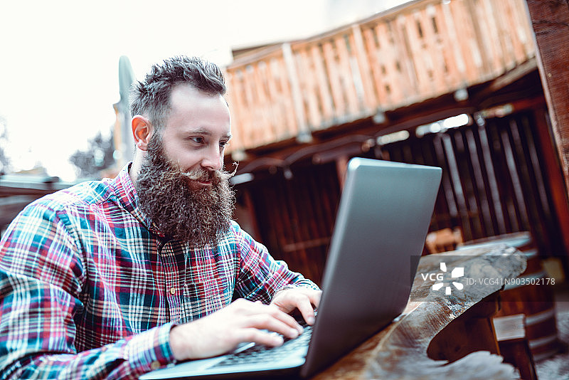 微笑的留胡子潮人自由职业者在他最喜欢的咖啡馆工作图片素材