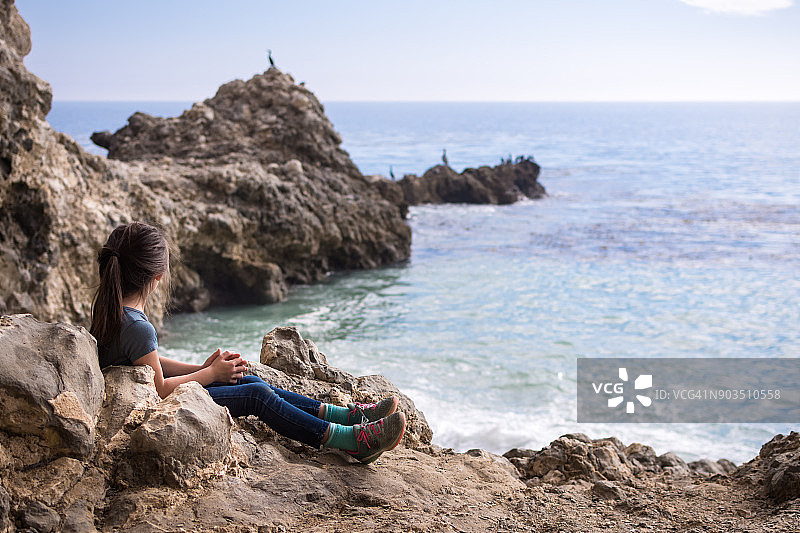 坐在帕洛斯弗迪牧场岩石海岸线上的女孩，加利福尼亚州图片素材