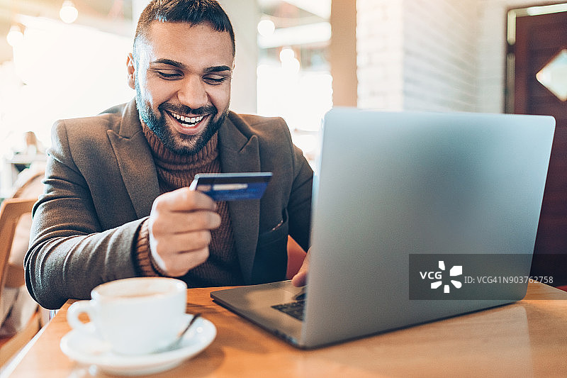 在咖啡馆里用笔记本电脑和信用卡的年轻男人图片素材