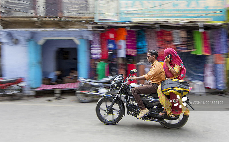 男人和女人穿着纱丽骑着摩托车在印度城市乌代布尔的街道上打电话图片素材