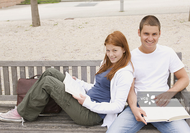 青少年情侣坐在长椅上阅读书籍图片素材