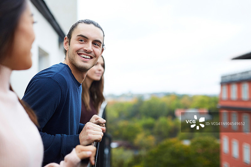 在城市阳台上与女性朋友站在一起的微笑的年轻男人图片素材