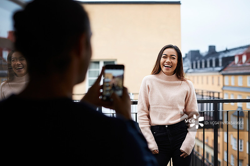 男人在阳台上用手机拍摄微笑的女友图片素材