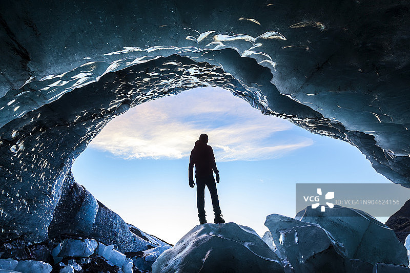站在冰洞入口的冰岩上的人的背影图片素材