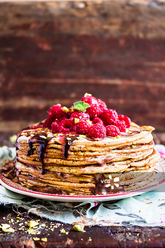 一叠小麦金黄薄烤饼或薄烤饼蛋糕，配以新鲜采摘的覆盆子、切碎的开心果、巧克力酱，选择性焦点图片素材