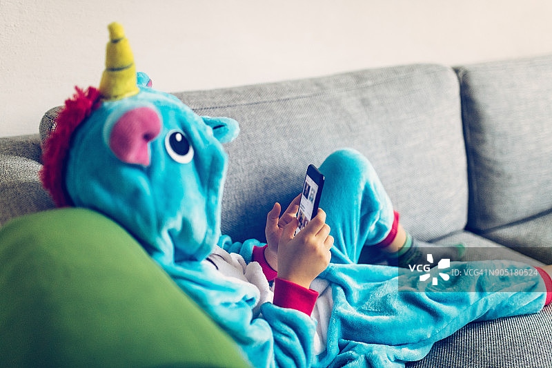 穿独角兽服装，在沙发上玩手机的小女孩图片素材