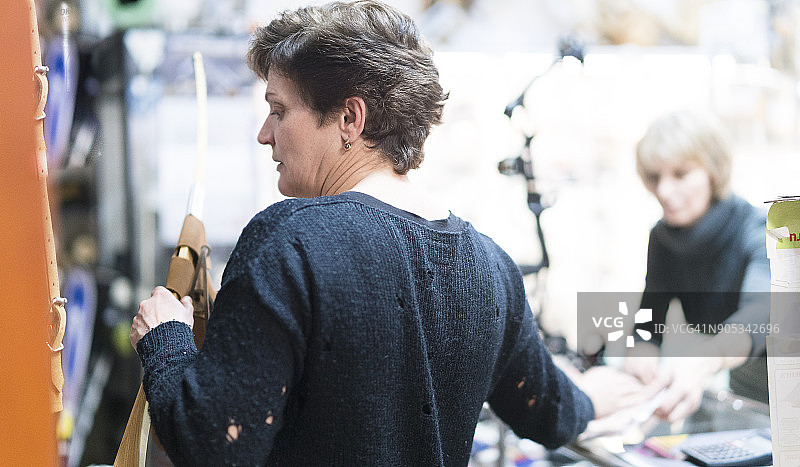 一位有魅力的金发中年妇女在狩猎商店里挑选弓箭，俄罗斯加里宁格勒，东欧图片素材