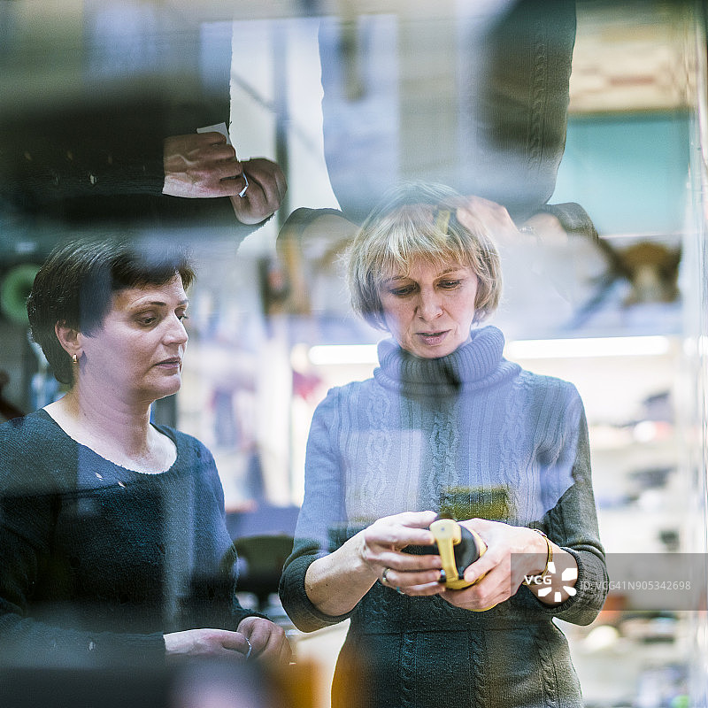 一位50岁的有魅力的中年妇女在小商店里购买商品，在店主的帮助下。图片素材