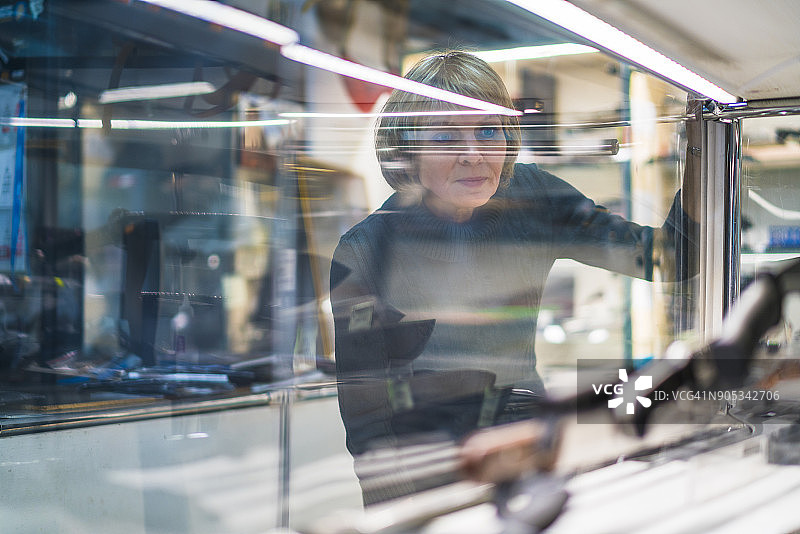 50岁成熟有魅力的女人在玻璃展柜中观看刀具收藏图片素材
