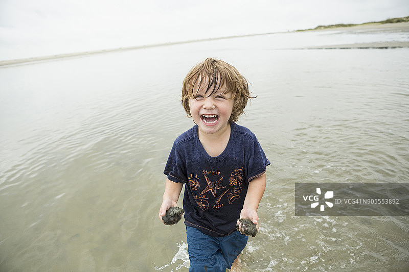 在海边拿着沙子等待的白人男孩图片素材