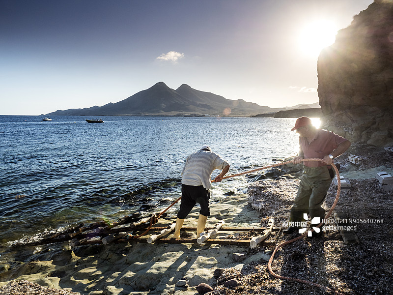 渔民在海中拉绳子，将船从水中拉出。用木头建造的传统渔船搁浅在西班牙阿尔梅里亚尼哈尔角加塔自然公园海滩的沙滩上图片素材