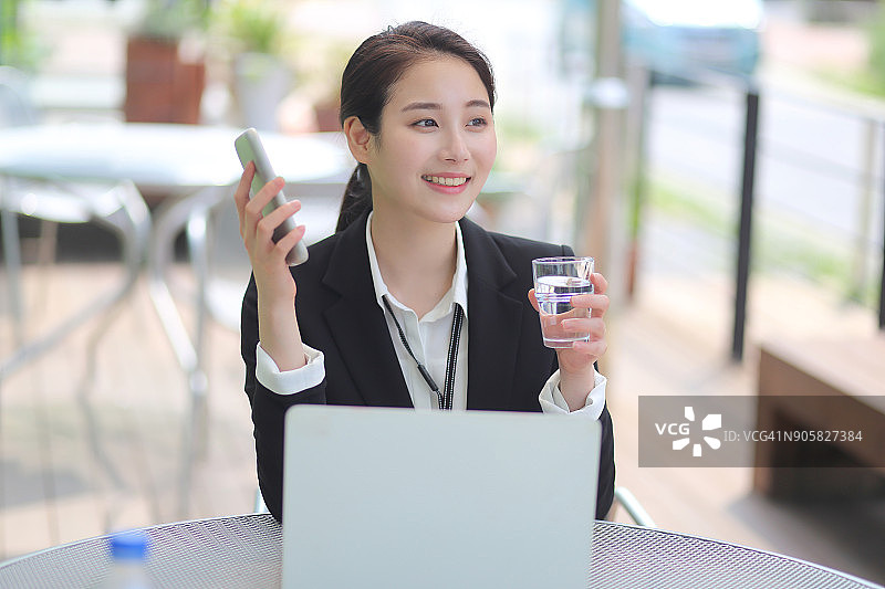 在咖啡馆里拿着智能手机和一杯水的女商人图片素材