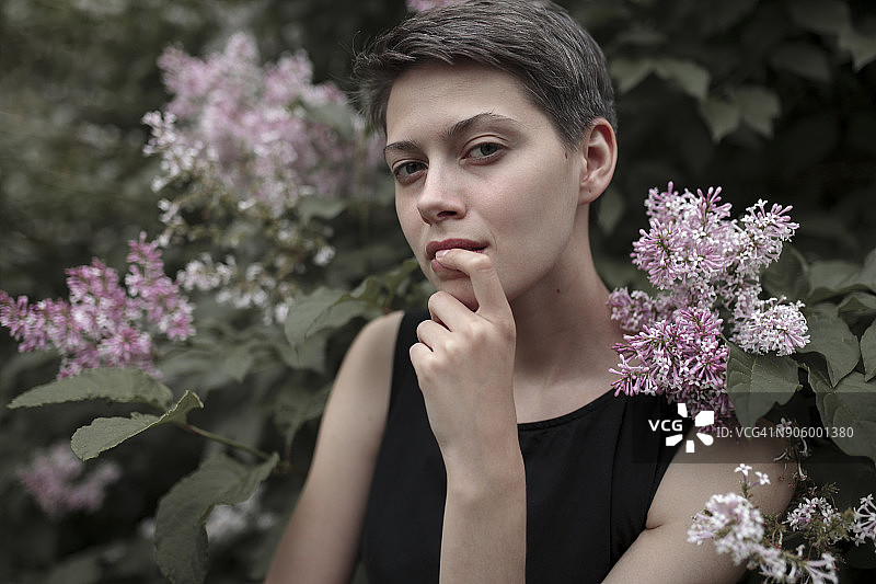 好奇的白人妇女在开花的树旁，手指放在嘴唇上图片素材
