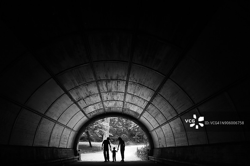 隧道中手牵着手的远处情侣和儿子图片素材