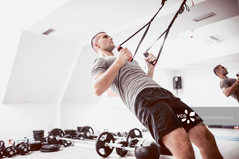 年轻运动员在健身房利用悬挂带做背部训练图片素材