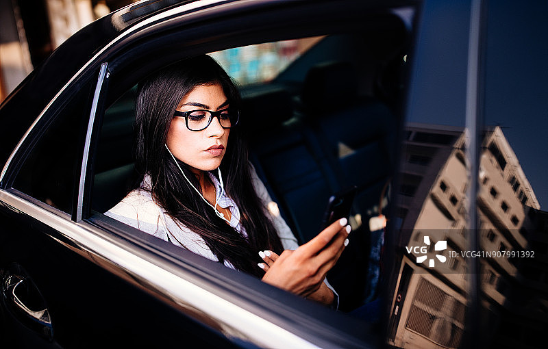 坐在黑色豪华轿车里使用智能手机的年轻女商人图片素材