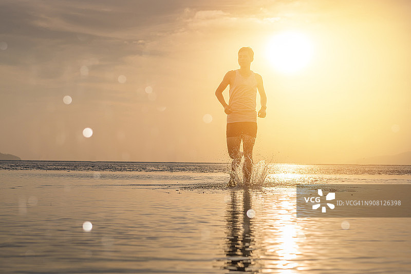 年轻的亚洲男人在海滩上跑步，背景是日落图片素材