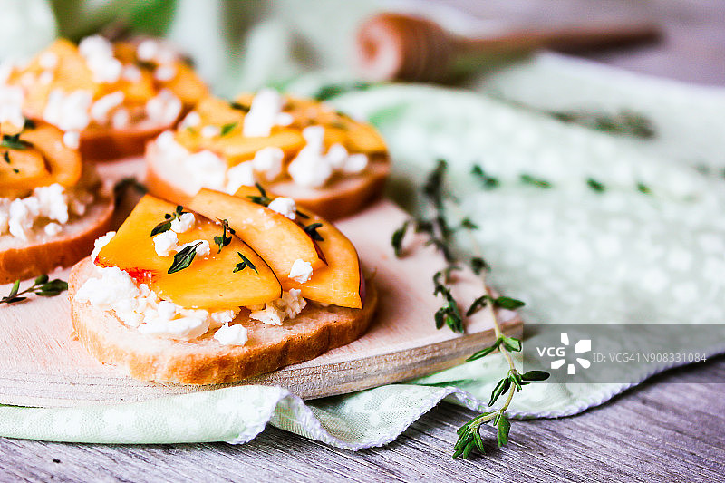 木板上的自制意大利烤面包，配油桃、盐渍菲达奶酪、干燥百里香和蜂蜜，选择性聚焦图片素材