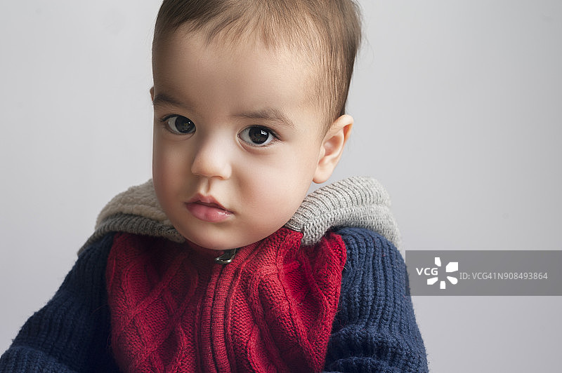 在工作室里表情严肃的穿红蓝毛衣的幼儿图片素材