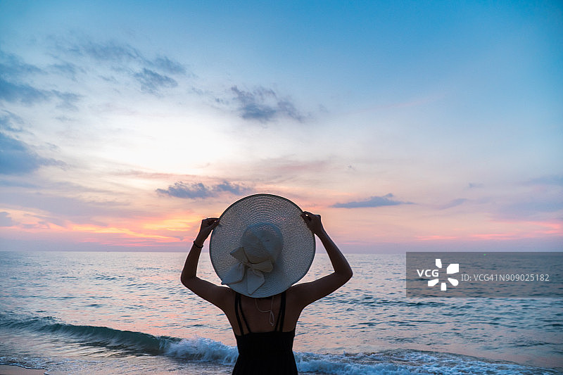 女人手拿白色帽子，眺望日落后的地平线图片素材