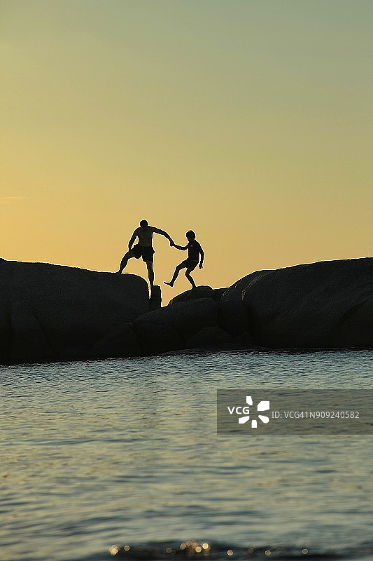 父亲帮助儿子在海边攀岩的剪影图片素材