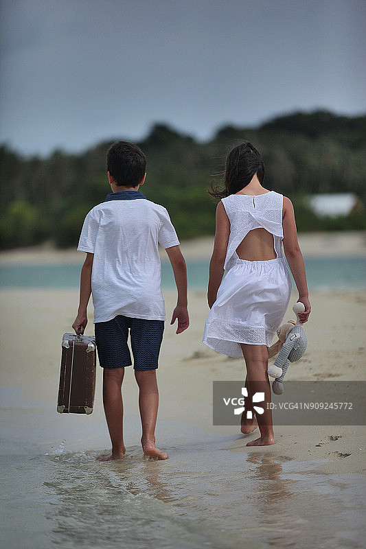 男孩和女孩在阴天的海滩上赤脚行走图片素材