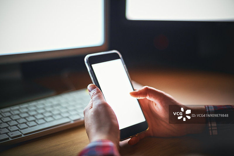 男人用手机，背景是两台电脑图片素材