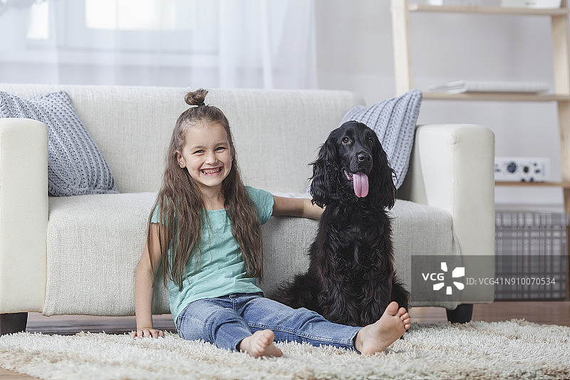 坐在家用地毯上的可爱女孩与可卡犬的肖像图片素材