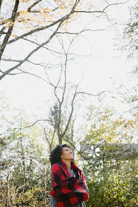 秋天在公园里抬头看树的微笑女性图片素材