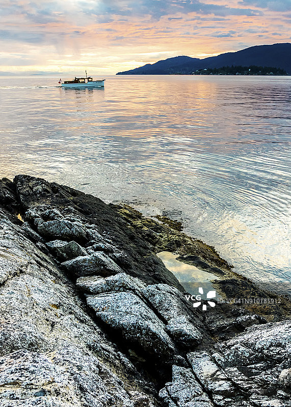 加拿大不列颠哥伦比亚省西温哥华灯塔公园的岩石海岸线和日落时分的摩托艇图片素材