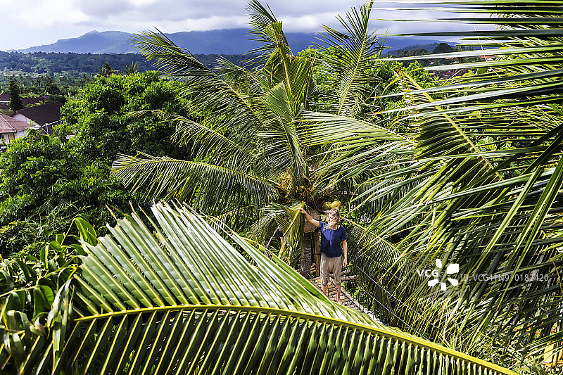 成年女人站在印度尼西亚巴厘岛棕榈树之间的绳索桥上图片素材