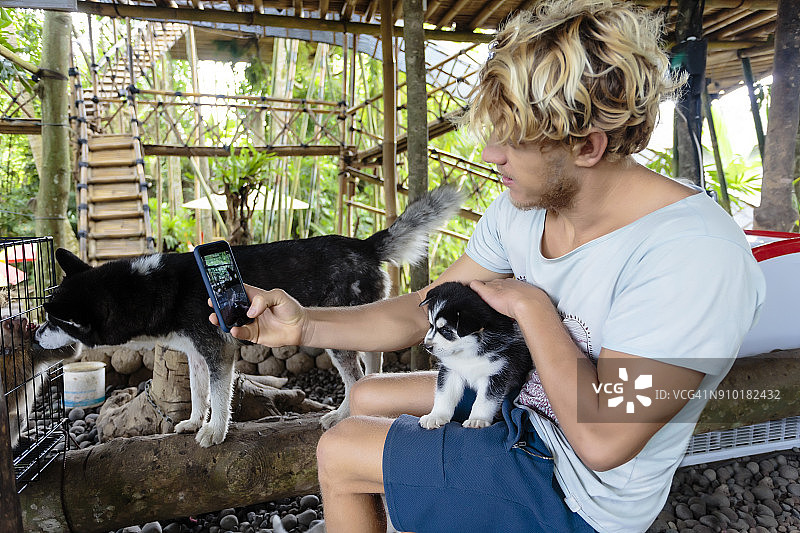 男人在印度尼西亚巴厘岛的竹屋里用手机和幼犬自拍图片素材