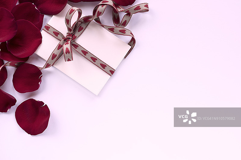 白色背景上心形丝带框住的红色玫瑰花瓣和空白便笺俯视图图片素材