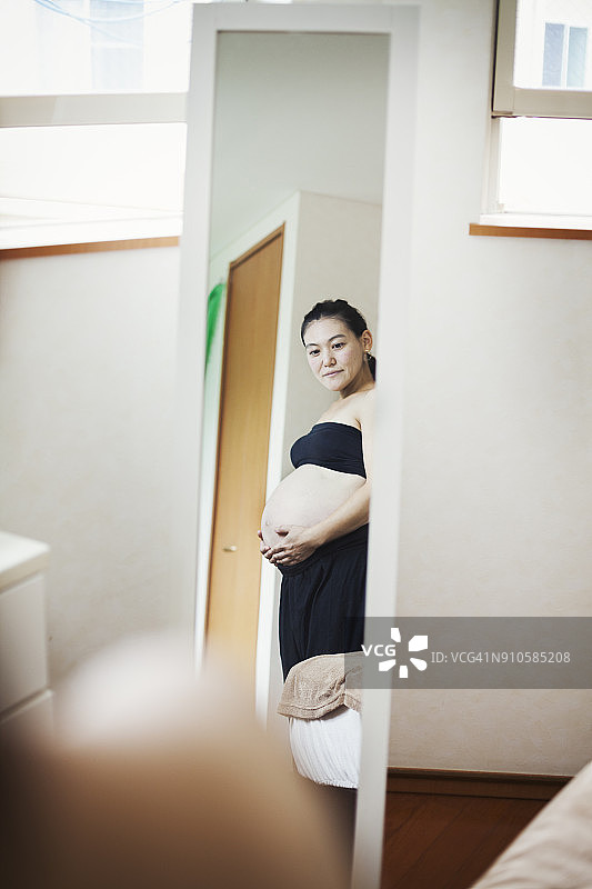 孕妇站在镜子前，双手放在腹部图片素材
