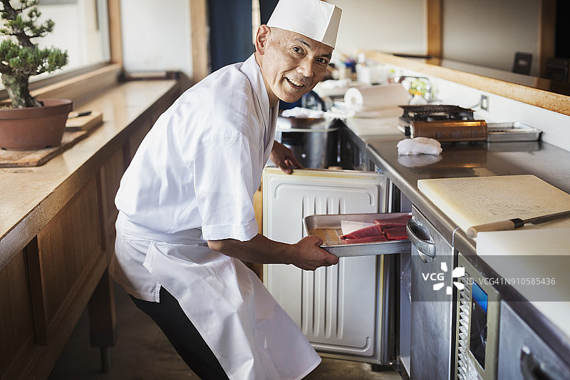 厨师在日式寿司店柜台工作，将装有鱼的金属托盘放入冰箱图片素材