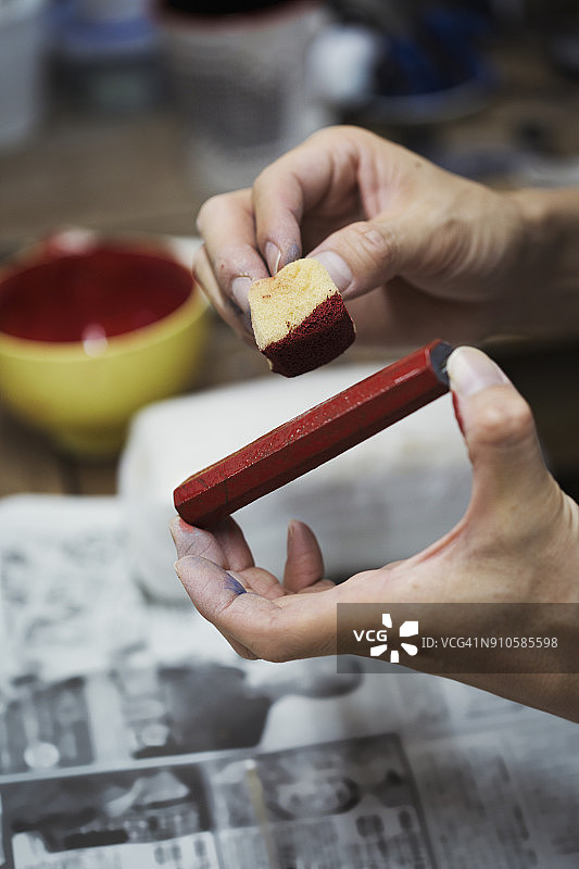 在日本瓷器作坊工作的女人特写，手持红色颜料棒和海绵图片素材