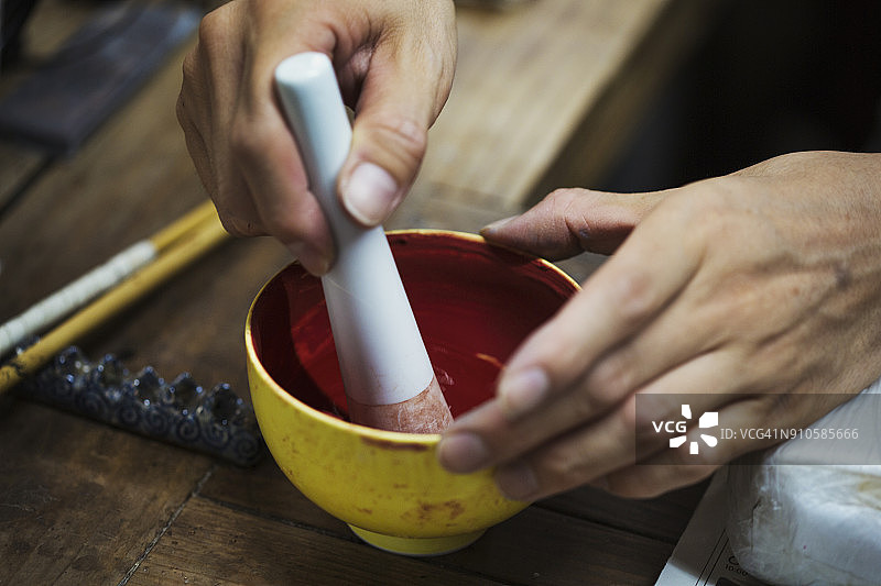 日本瓷器工坊工人用研钵和杵混合红色颜料特写图片素材